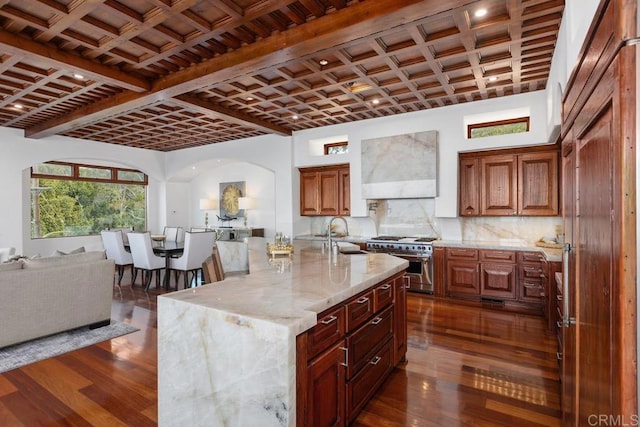 kitchen featuring wall chimney exhaust hood, coffered ceiling, sink, a center island with sink, and double oven range