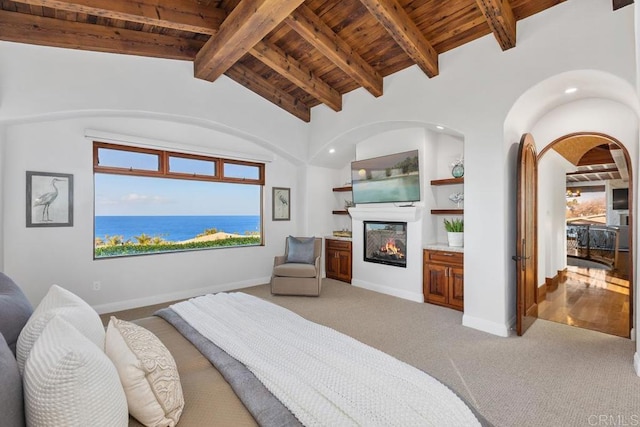 carpeted bedroom with a glass covered fireplace, vaulted ceiling with beams, baseboards, and wooden ceiling