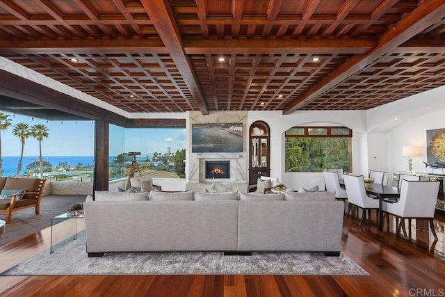 living area with a wealth of natural light, a large fireplace, beamed ceiling, and wood finished floors