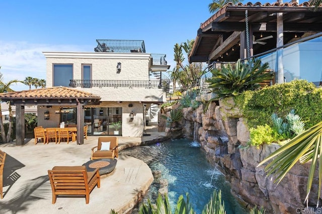 back of house featuring a balcony, an outdoor living space, an outdoor pool, a patio area, and a garden pond