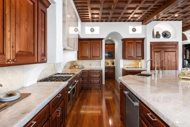 kitchen featuring light stone counters, coffered ceiling, dark wood finished floors, appliances with stainless steel finishes, and a sink
