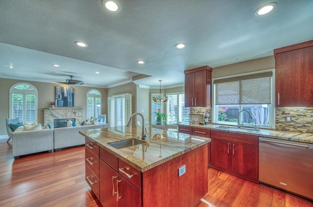 kitchen featuring light stone counters, sink, an island with sink, and dishwasher