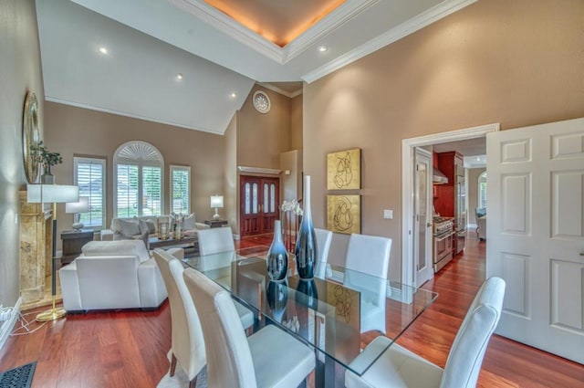 dining area with hardwood / wood-style floors, a tray ceiling, ornamental molding, and high vaulted ceiling