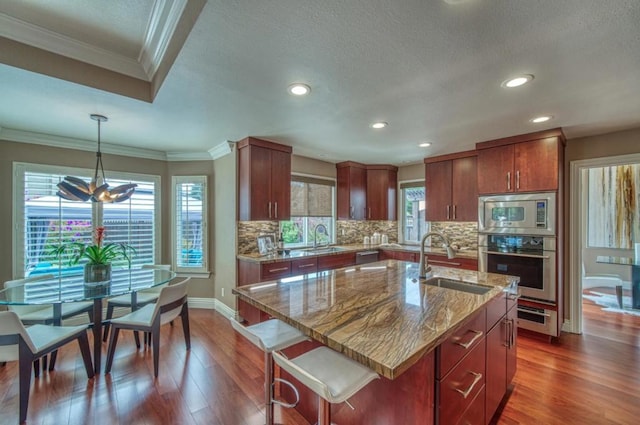 kitchen featuring sink, hanging light fixtures, stainless steel appliances, dark hardwood / wood-style floors, and an island with sink