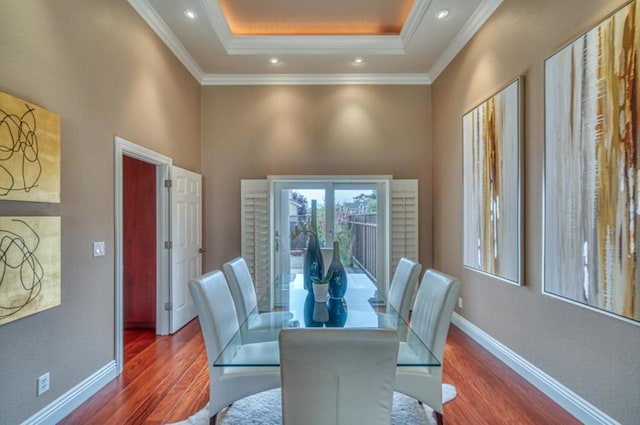 dining room with a tray ceiling, hardwood / wood-style flooring, ornamental molding, and a high ceiling