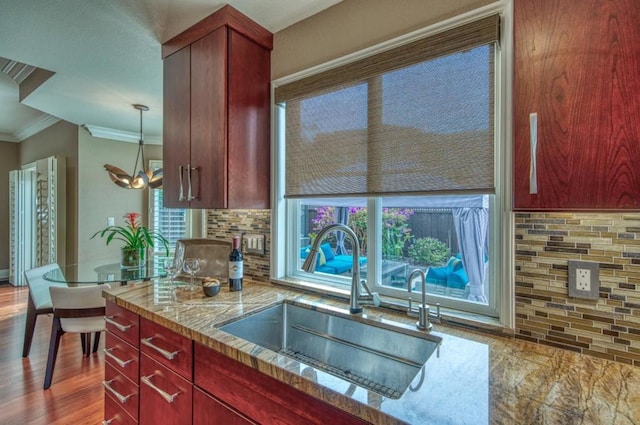 kitchen with sink, hanging light fixtures, ornamental molding, light stone countertops, and backsplash