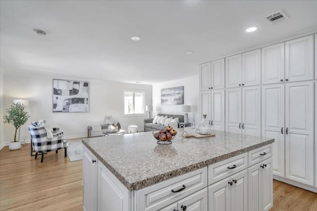 kitchen with light stone countertops, a center island, white cabinets, and light hardwood / wood-style floors