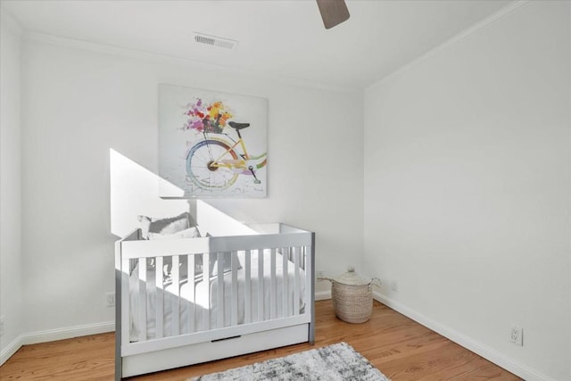 bedroom with a nursery area, ceiling fan, crown molding, and hardwood / wood-style floors