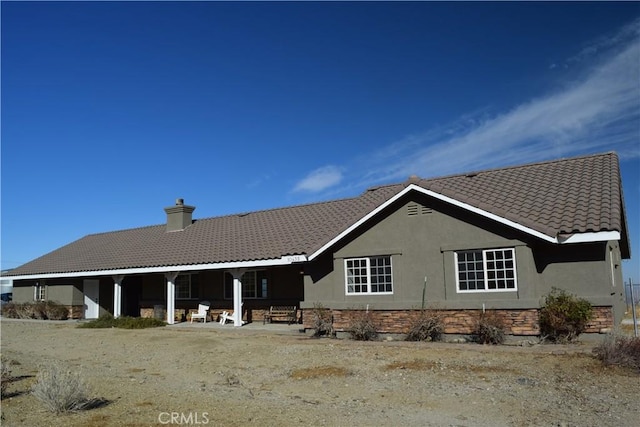 back of property featuring a tiled roof, a chimney, a patio, and stucco siding