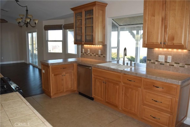 kitchen with tile countertops, glass insert cabinets, a peninsula, stainless steel dishwasher, and a sink