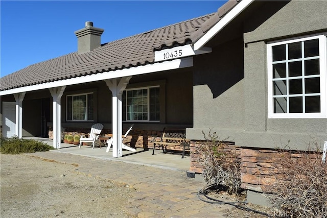 rear view of house featuring stucco siding, a tiled roof, a chimney, and a patio