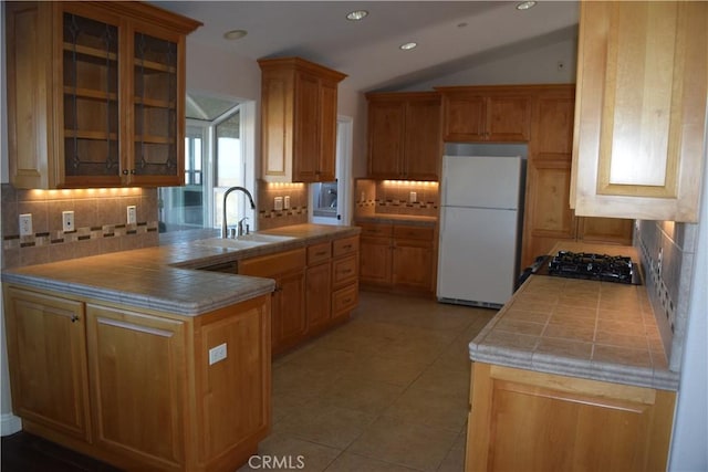 kitchen with tile countertops, glass insert cabinets, a sink, and freestanding refrigerator