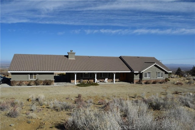 rear view of property featuring a tile roof, a chimney, and stucco siding