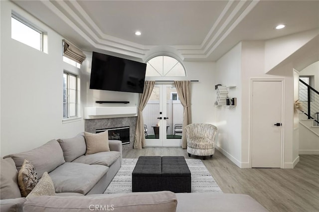 living room with french doors, a high end fireplace, a tray ceiling, and light wood-type flooring