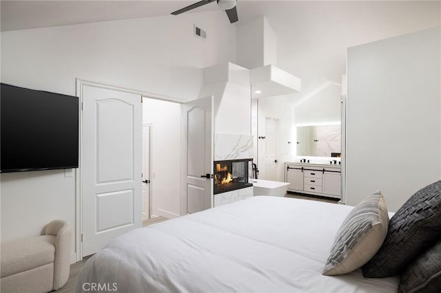 bedroom with ensuite bath, high vaulted ceiling, ceiling fan, a high end fireplace, and hardwood / wood-style floors