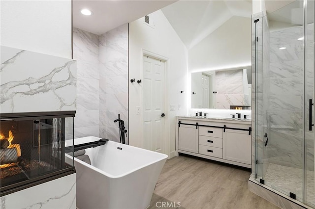 bathroom with lofted ceiling, vanity, a fireplace, wood-type flooring, and shower with separate bathtub