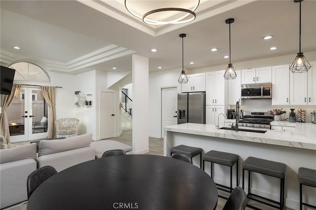 kitchen featuring appliances with stainless steel finishes, tasteful backsplash, white cabinets, light stone counters, and a tray ceiling