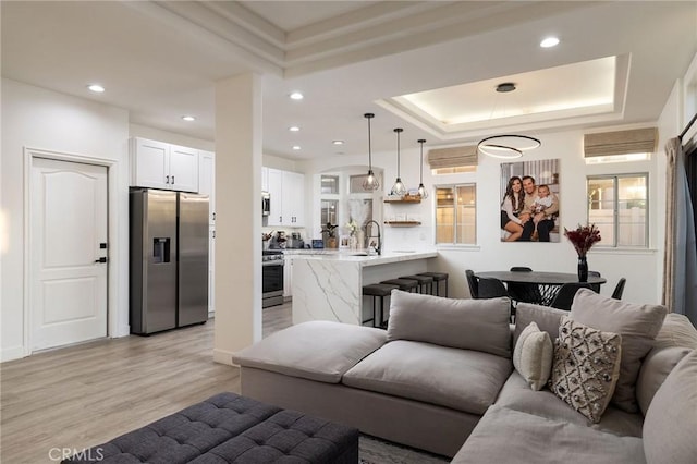 living room with a raised ceiling, sink, and light wood-type flooring