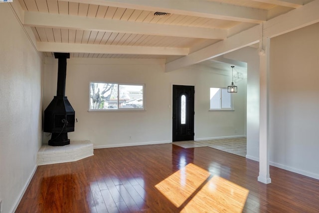 unfurnished living room featuring hardwood / wood-style flooring, lofted ceiling with beams, and a wood stove