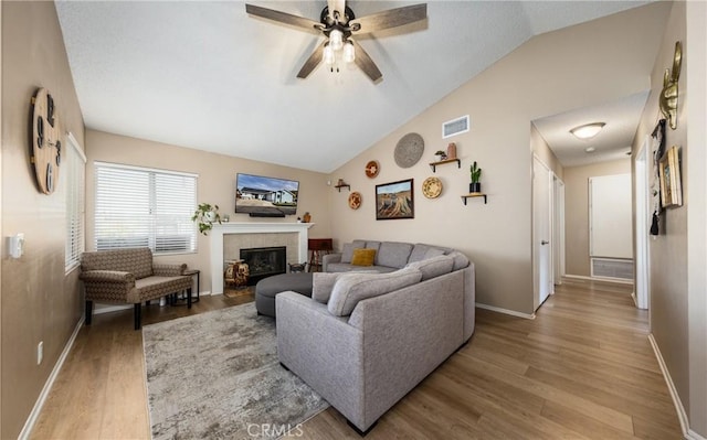 living room featuring ceiling fan, lofted ceiling, a tile fireplace, and wood-type flooring