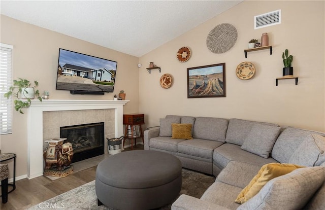 living room featuring a tile fireplace, lofted ceiling, and hardwood / wood-style floors