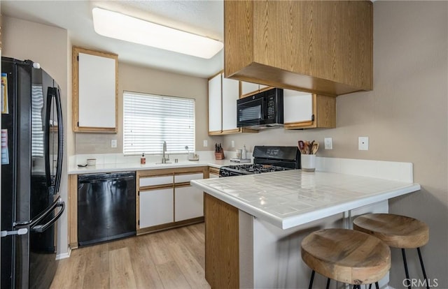 kitchen featuring black appliances, white cabinets, a kitchen bar, tile counters, and kitchen peninsula