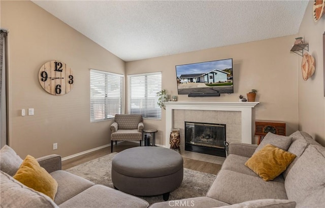 living room with vaulted ceiling, a tile fireplace, light hardwood / wood-style floors, and a textured ceiling