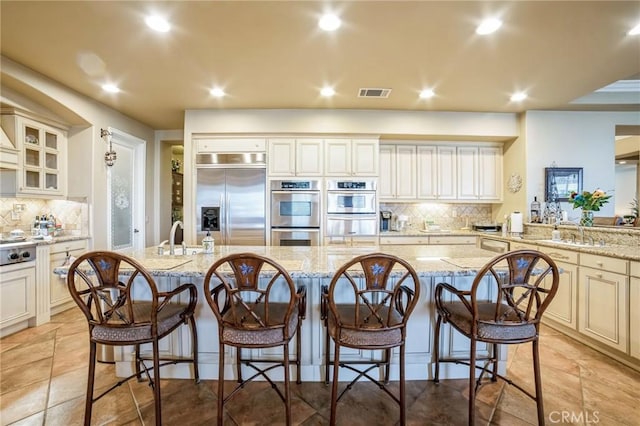 kitchen with a center island with sink, light stone countertops, and appliances with stainless steel finishes