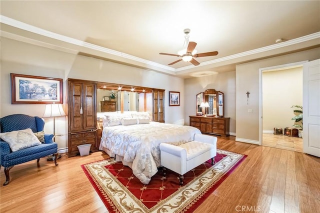 bedroom with wood-type flooring, ornamental molding, ceiling fan, and a tray ceiling