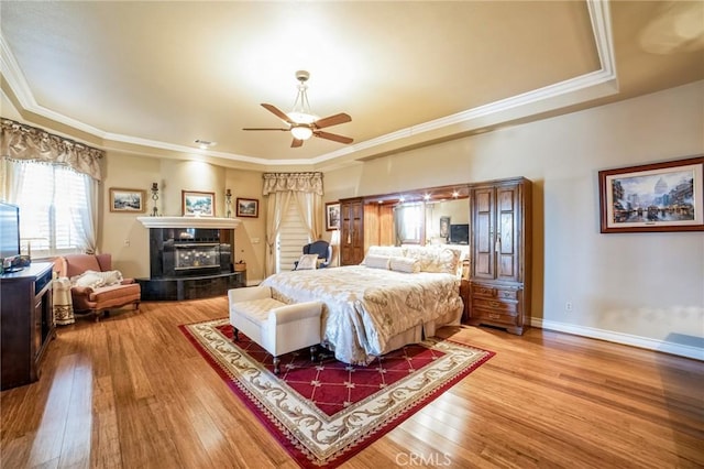 bedroom with hardwood / wood-style flooring, a tray ceiling, a tile fireplace, and crown molding