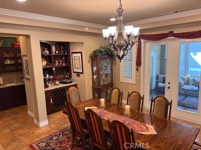 dining area with ornamental molding, indoor bar, and a notable chandelier