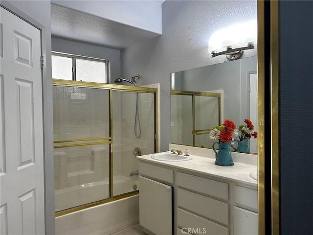 bathroom featuring vanity, a textured ceiling, and combined bath / shower with glass door