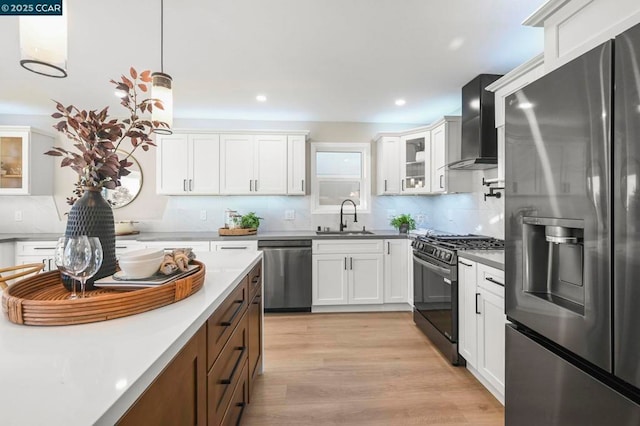 kitchen with wall chimney exhaust hood, sink, appliances with stainless steel finishes, pendant lighting, and white cabinets