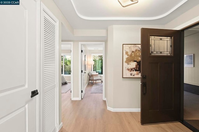 hall with a tray ceiling and light wood-type flooring