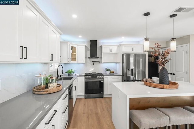 kitchen featuring sink, a breakfast bar area, white cabinets, stainless steel appliances, and wall chimney range hood