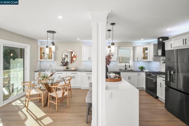 kitchen with pendant lighting, stainless steel fridge with ice dispenser, wall chimney range hood, and range with gas stovetop