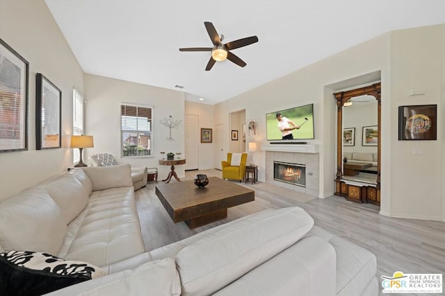 living room with a tiled fireplace, light hardwood / wood-style floors, and ceiling fan