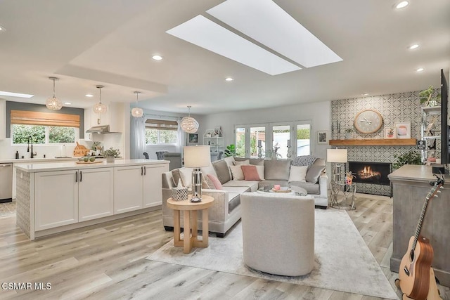 living room featuring sink, a large fireplace, light hardwood / wood-style flooring, and a skylight