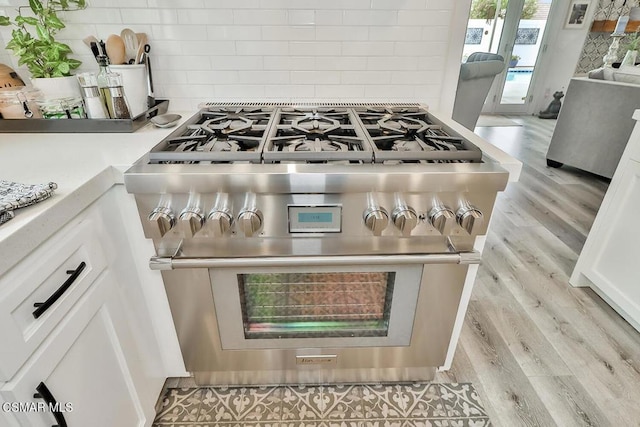 interior details with white cabinetry, high end stainless steel range, tasteful backsplash, and light hardwood / wood-style flooring