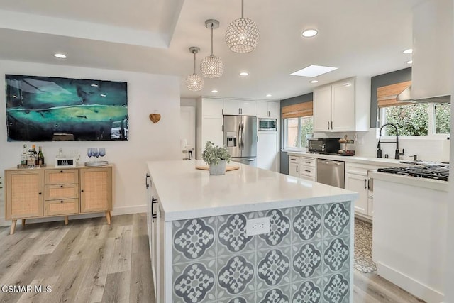 kitchen featuring light hardwood / wood-style flooring, appliances with stainless steel finishes, hanging light fixtures, white cabinets, and decorative backsplash