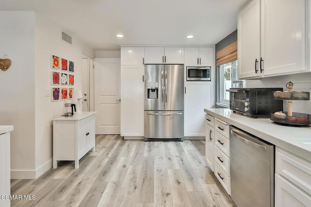 kitchen with white cabinetry, stainless steel appliances, decorative backsplash, and light wood-type flooring