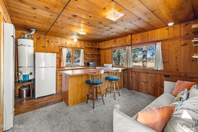 kitchen featuring secured water heater, a kitchen breakfast bar, white fridge, wooden ceiling, and wood walls