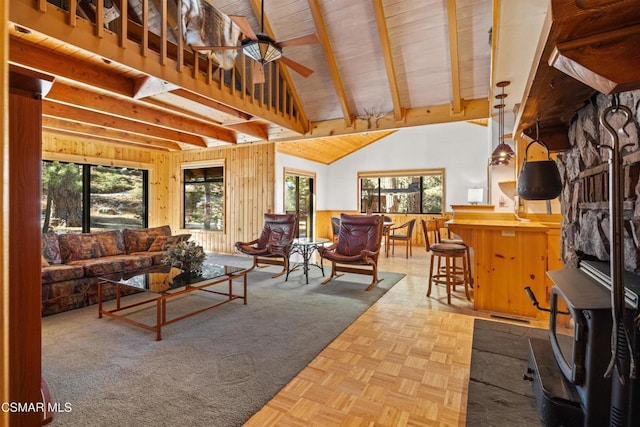 living room featuring vaulted ceiling with beams, wooden walls, light parquet flooring, and ceiling fan