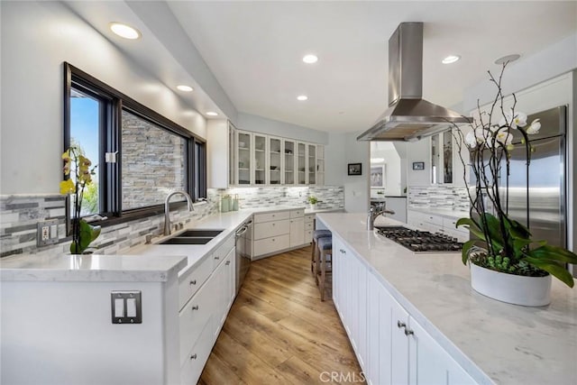 kitchen featuring stainless steel appliances, white cabinetry, island exhaust hood, and sink