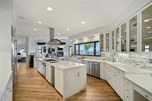 kitchen featuring island range hood, an island with sink, white cabinets, light stone counters, and stainless steel appliances