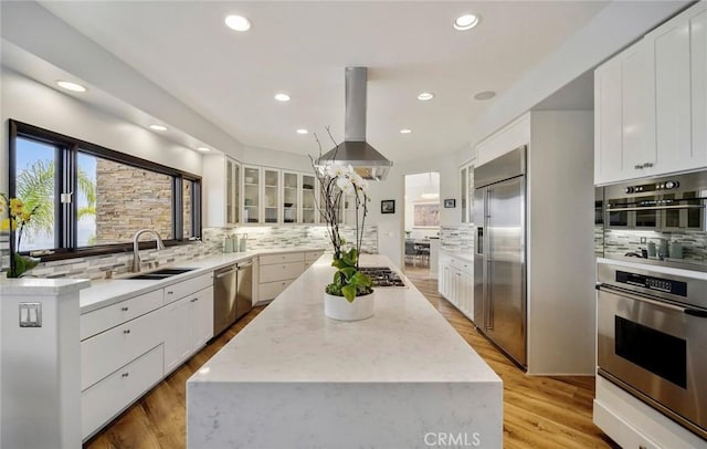 kitchen featuring sink, island range hood, light hardwood / wood-style flooring, stainless steel appliances, and white cabinets