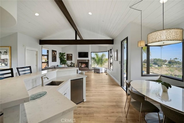 kitchen with dishwashing machine, sink, lofted ceiling with beams, light hardwood / wood-style floors, and decorative light fixtures