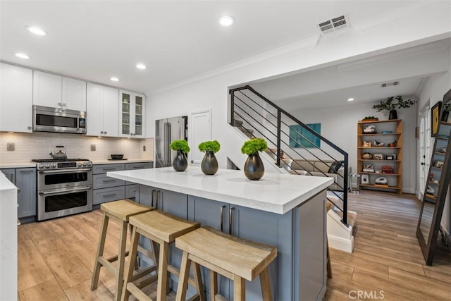 kitchen with a breakfast bar area, gray cabinetry, appliances with stainless steel finishes, a kitchen island, and white cabinets