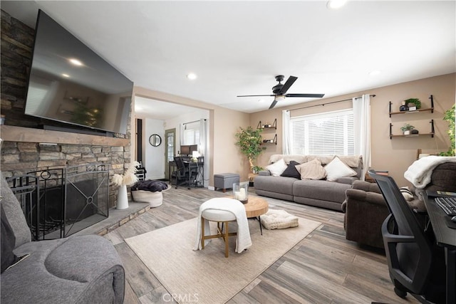 living room with ceiling fan, a stone fireplace, and light hardwood / wood-style floors