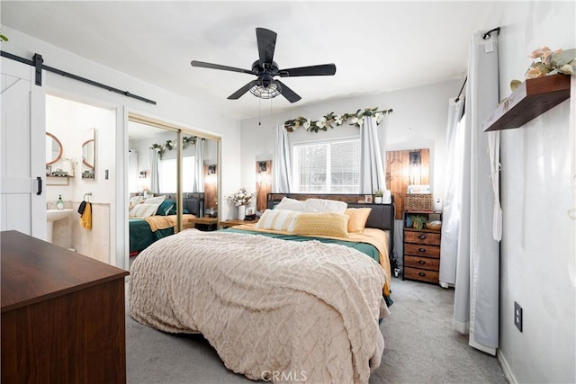 bedroom featuring ceiling fan, ensuite bathroom, a barn door, light carpet, and a closet